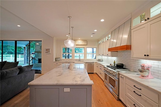 kitchen with white cabinets, a kitchen island, stainless steel appliances, hanging light fixtures, and light stone counters