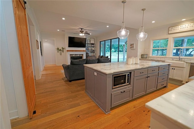 kitchen featuring a center island, hanging light fixtures, light stone counters, stainless steel microwave, and gray cabinetry