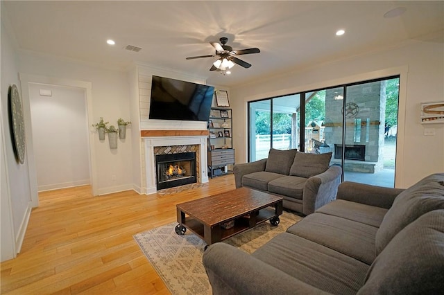 living room with light hardwood / wood-style floors, crown molding, and a tiled fireplace