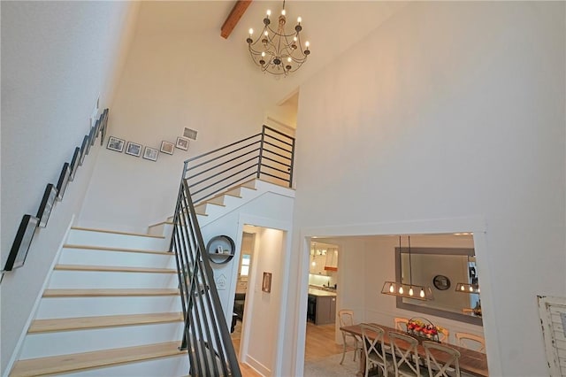 stairway with an inviting chandelier, beamed ceiling, and a high ceiling