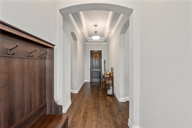 hallway featuring a tray ceiling, dark wood finished floors, arched walkways, crown molding, and baseboards