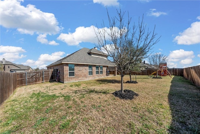 rear view of house featuring a lawn, a fenced backyard, brick siding, and a playground