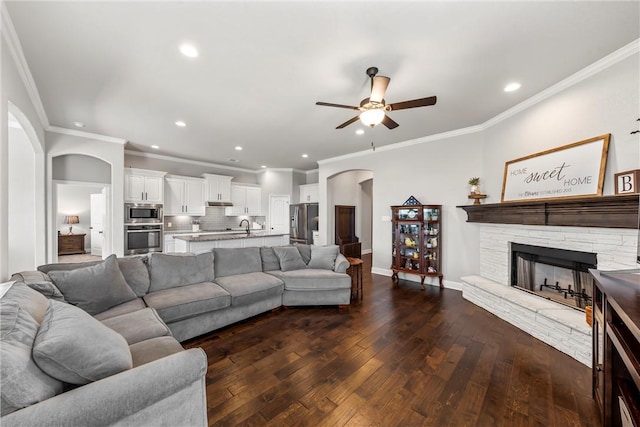 living room with dark wood-type flooring, recessed lighting, arched walkways, a stone fireplace, and baseboards