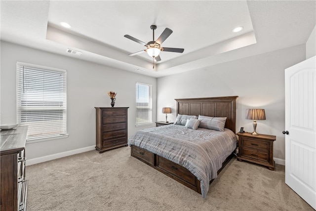 bedroom with light colored carpet, a tray ceiling, baseboards, and visible vents