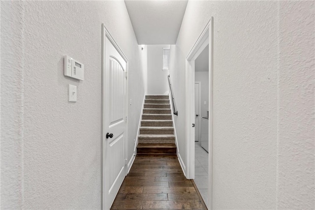 corridor featuring stairs, a textured wall, and dark wood-style flooring