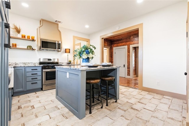 kitchen with a kitchen bar, appliances with stainless steel finishes, a center island, and light stone counters