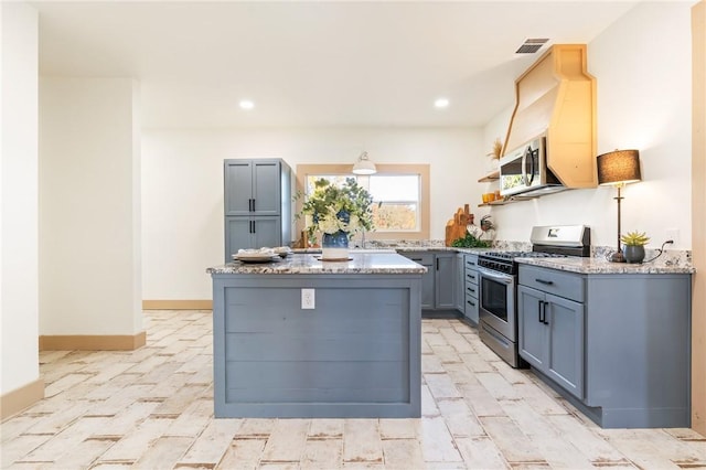 kitchen with gray cabinets, a center island, stainless steel appliances, and light stone countertops