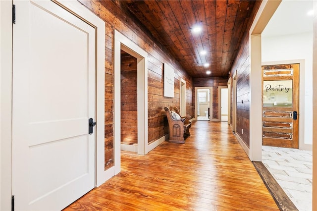 corridor featuring wooden walls, light hardwood / wood-style flooring, and wooden ceiling