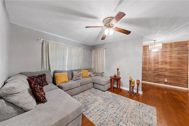 living room with wooden walls, hardwood / wood-style floors, and ceiling fan with notable chandelier