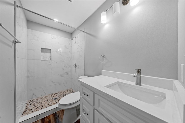 bathroom featuring vanity, toilet, a tile shower, and wood-type flooring