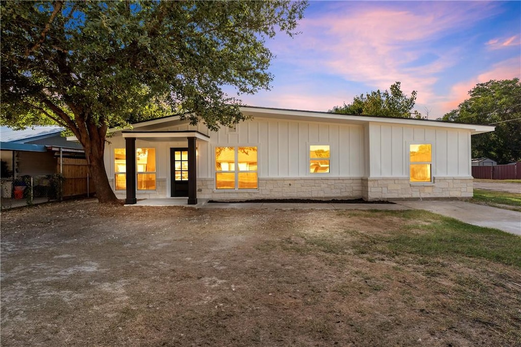 view of front of home featuring board and batten siding, fence, and stone siding