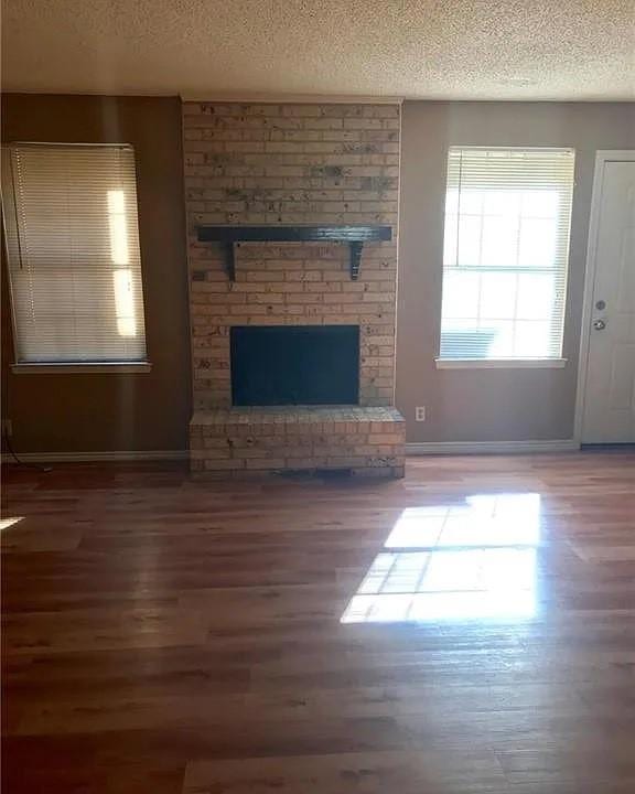 unfurnished living room with wood-type flooring, a brick fireplace, and a textured ceiling