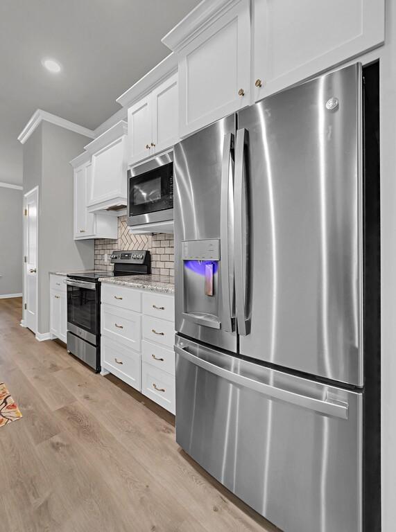 kitchen with light stone counters, stainless steel appliances, white cabinetry, tasteful backsplash, and crown molding