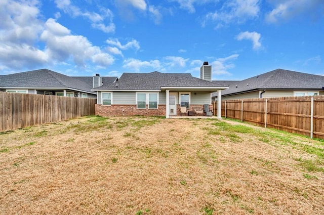 back of house featuring a patio, a fenced backyard, brick siding, a lawn, and a chimney