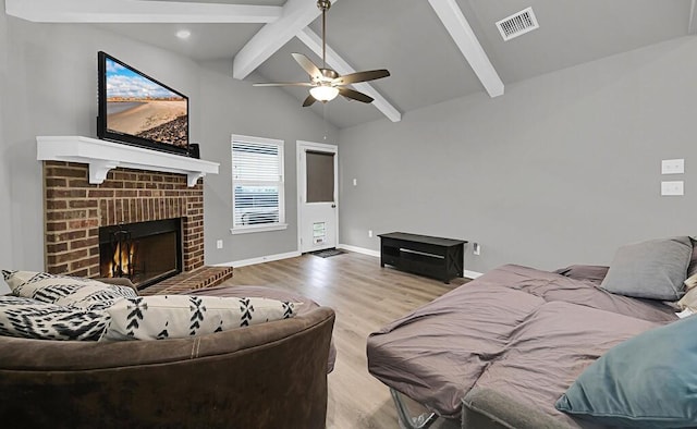 living area with visible vents, baseboards, vaulted ceiling with beams, light wood-type flooring, and a brick fireplace