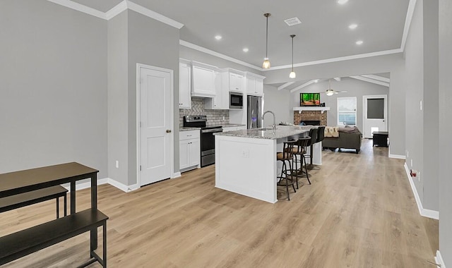 kitchen featuring open floor plan, decorative light fixtures, light stone countertops, stainless steel appliances, and white cabinetry