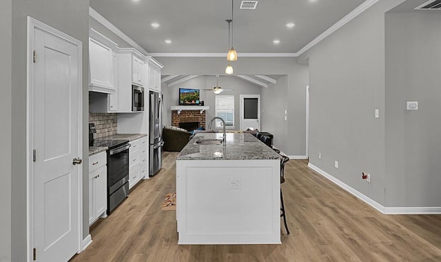 kitchen with appliances with stainless steel finishes, pendant lighting, white cabinets, and a center island with sink