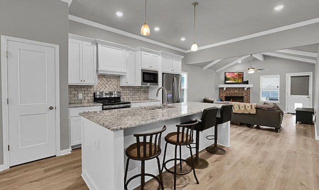 kitchen with stainless steel appliances, hanging light fixtures, open floor plan, a sink, and a kitchen breakfast bar