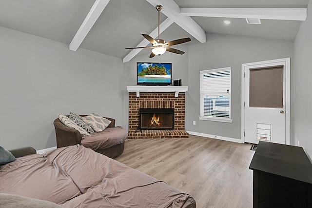 living area featuring vaulted ceiling with beams, light wood-style floors, a brick fireplace, ceiling fan, and baseboards