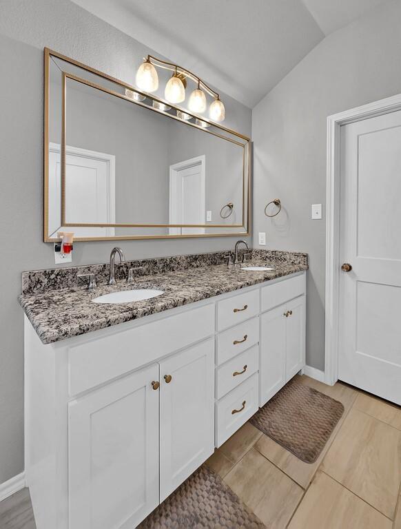 full bathroom featuring vaulted ceiling, double vanity, a sink, and baseboards