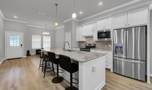 kitchen with a center island with sink, decorative light fixtures, stainless steel appliances, white cabinetry, and a sink