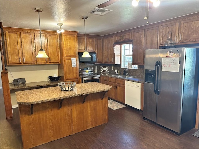 kitchen featuring appliances with stainless steel finishes, sink, pendant lighting, dark hardwood / wood-style floors, and a breakfast bar area