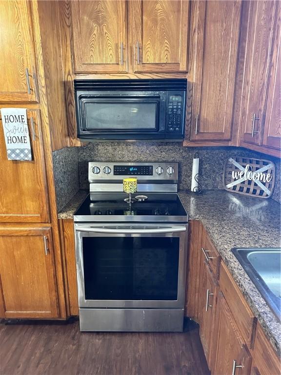 kitchen with stainless steel range with electric stovetop, dark stone counters, sink, decorative backsplash, and dark hardwood / wood-style flooring