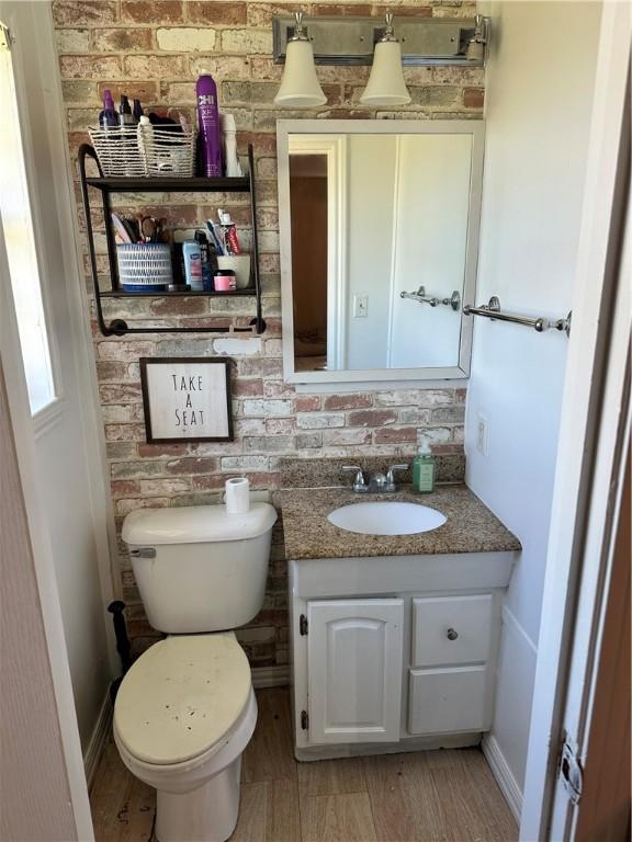 bathroom with hardwood / wood-style floors, vanity, toilet, and brick wall