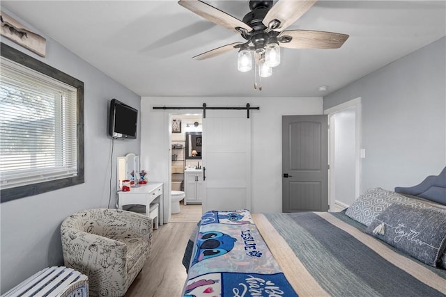 bedroom with connected bathroom, light hardwood / wood-style flooring, a barn door, and ceiling fan