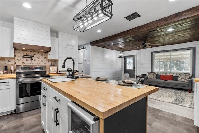 kitchen with an island with sink, stainless steel range with electric cooktop, wooden counters, and white cabinets