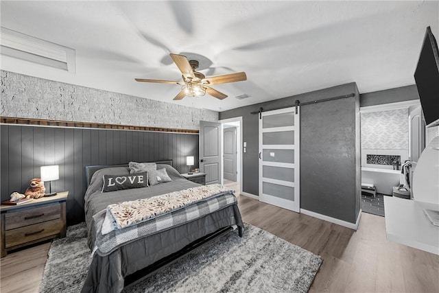 bedroom with ceiling fan, a barn door, and light wood-type flooring