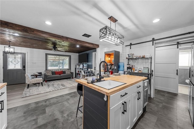 kitchen featuring decorative light fixtures, an island with sink, sink, white cabinets, and a barn door