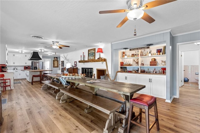 dining space featuring a large fireplace, crown molding, light hardwood / wood-style flooring, and a textured ceiling