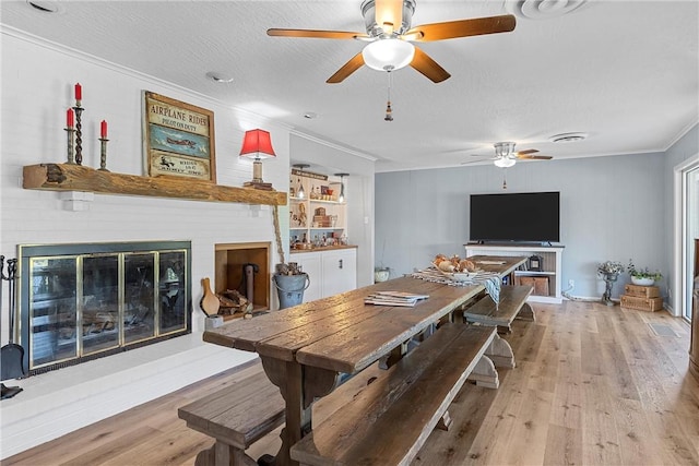 dining area featuring a textured ceiling, light hardwood / wood-style floors, crown molding, and a fireplace