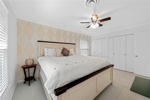 bedroom featuring ceiling fan, light colored carpet, ornamental molding, and two closets