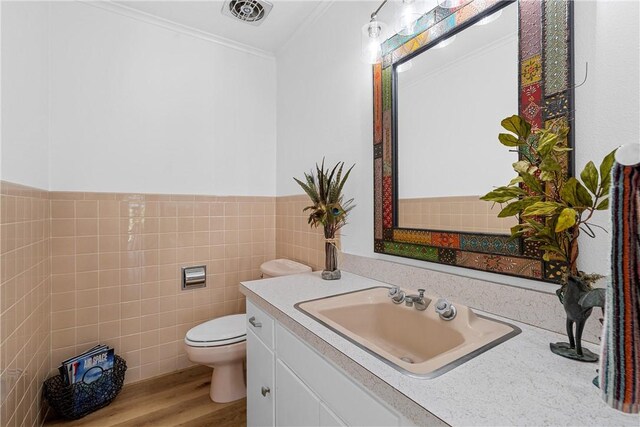 bathroom featuring vanity, hardwood / wood-style flooring, toilet, ornamental molding, and tile walls