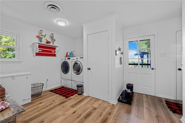 clothes washing area featuring a textured ceiling, light wood-type flooring, ornamental molding, and washing machine and clothes dryer