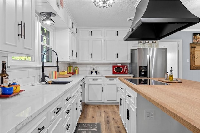 kitchen featuring sink, stainless steel fridge, extractor fan, white cabinets, and light wood-type flooring