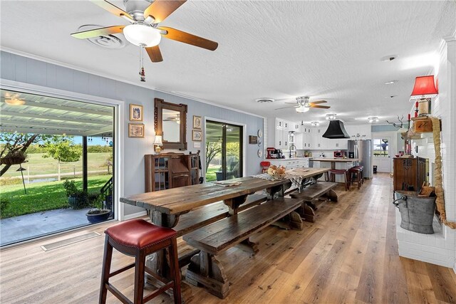 dining area with ceiling fan, light hardwood / wood-style flooring, a textured ceiling, and ornamental molding