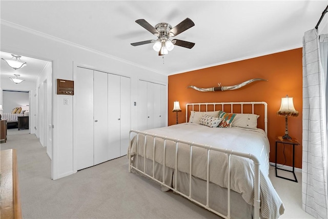 carpeted bedroom featuring two closets, ceiling fan, and crown molding