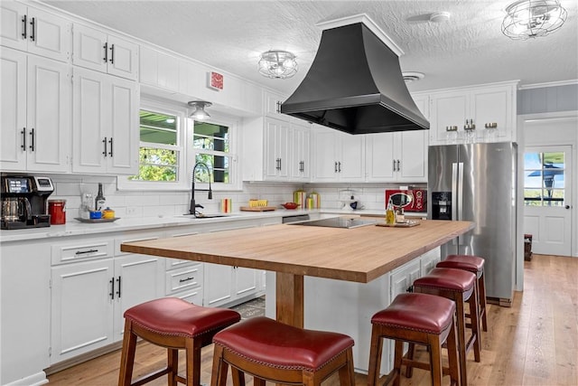 kitchen featuring island exhaust hood, stainless steel fridge, wooden counters, and white cabinetry