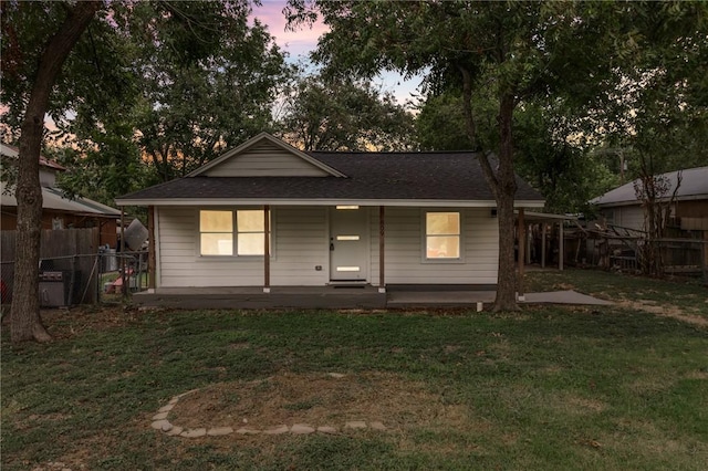 back house at dusk featuring a lawn and covered porch