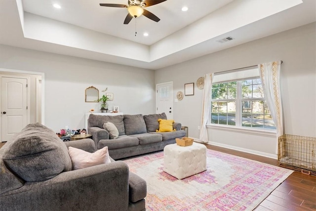 living room with a tray ceiling, ceiling fan, and dark hardwood / wood-style flooring