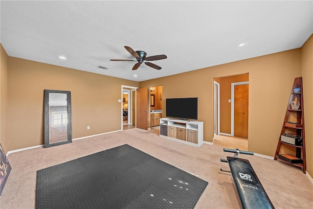 exercise room featuring light carpet, ceiling fan, and a textured ceiling