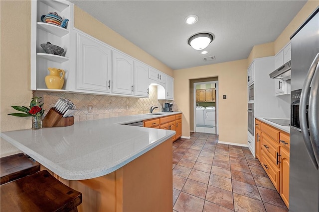 kitchen with kitchen peninsula, a kitchen bar, exhaust hood, washing machine and dryer, and white cabinetry