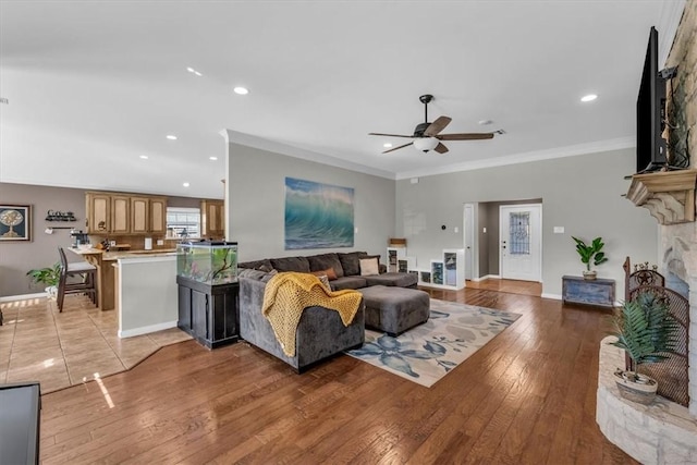 living room featuring light hardwood / wood-style floors, a stone fireplace, ceiling fan, and crown molding