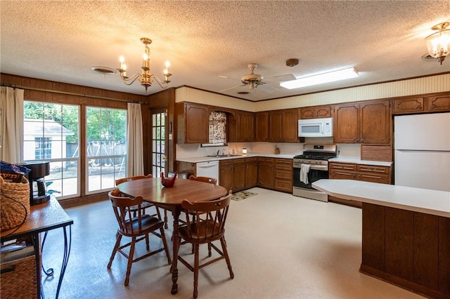 kitchen featuring a textured ceiling, white appliances, light countertops, hanging light fixtures, and brown cabinets