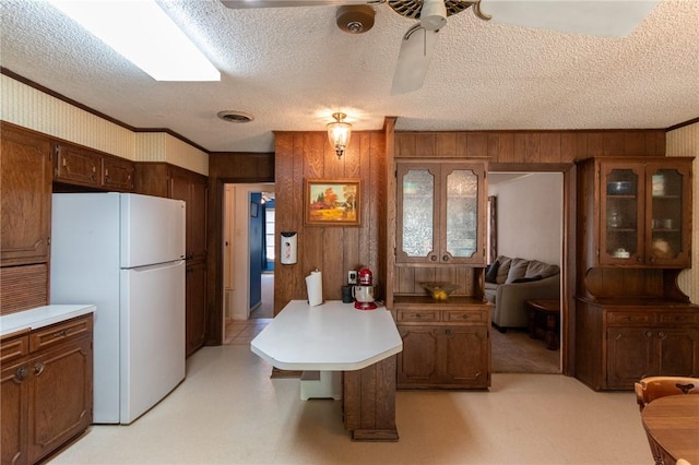 kitchen with light countertops, visible vents, freestanding refrigerator, wood walls, and a textured ceiling