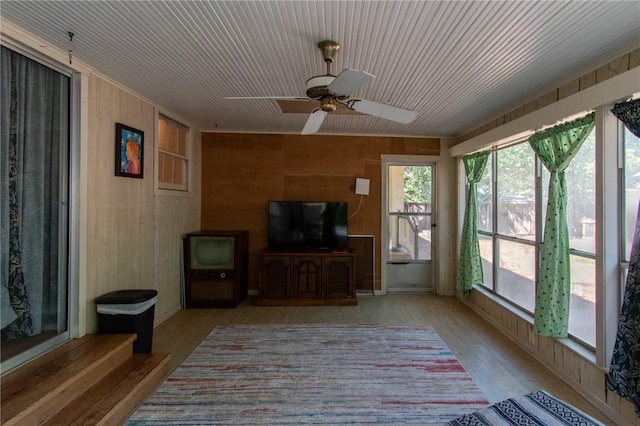 living room featuring light wood-style floors, wooden walls, and a ceiling fan