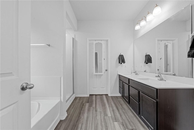 bathroom with double vanity, wood finished floors, a sink, and a bath